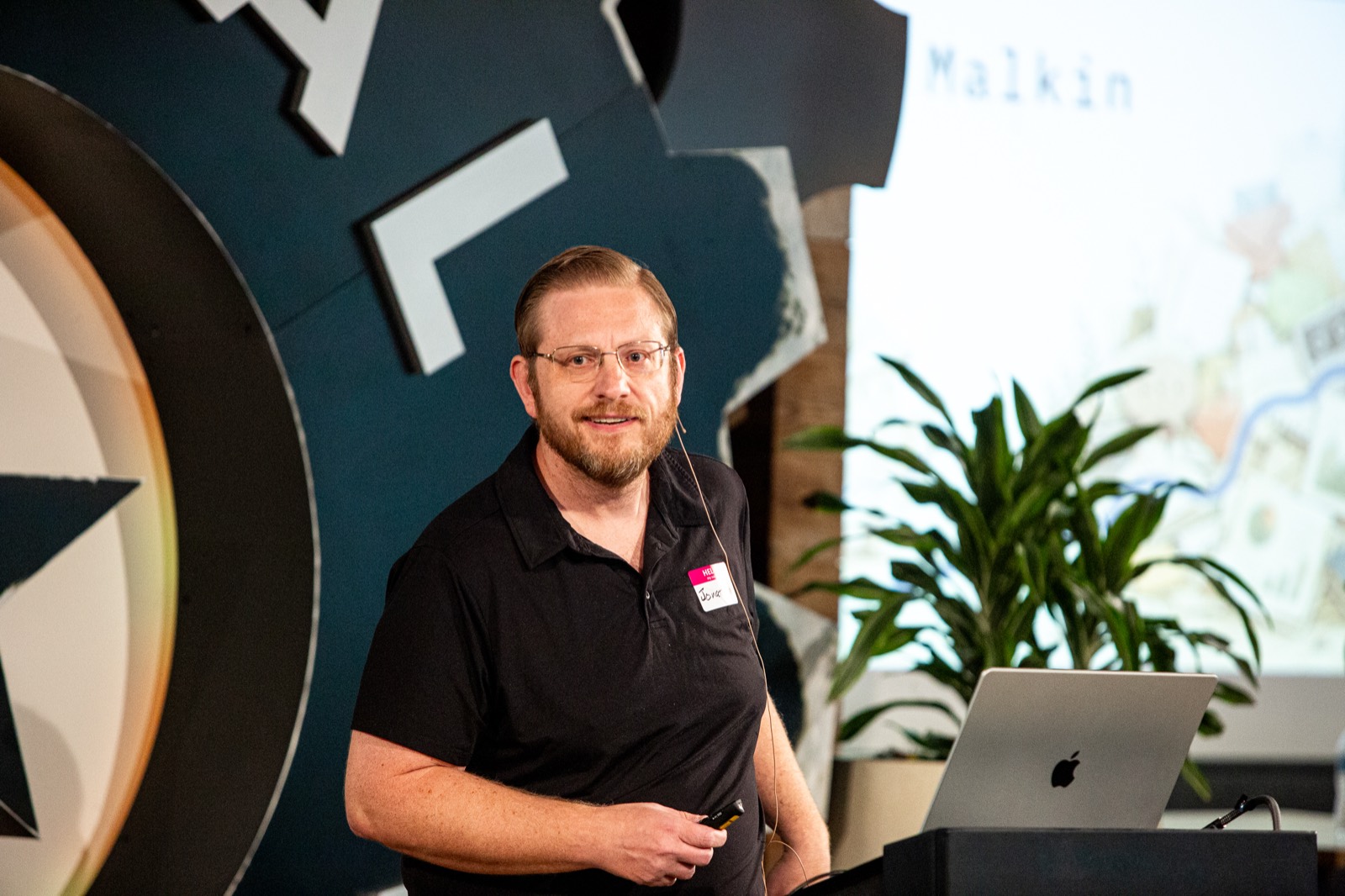 Jonathan Malkin presenting beside a laptop, with his name on the screen behind him.