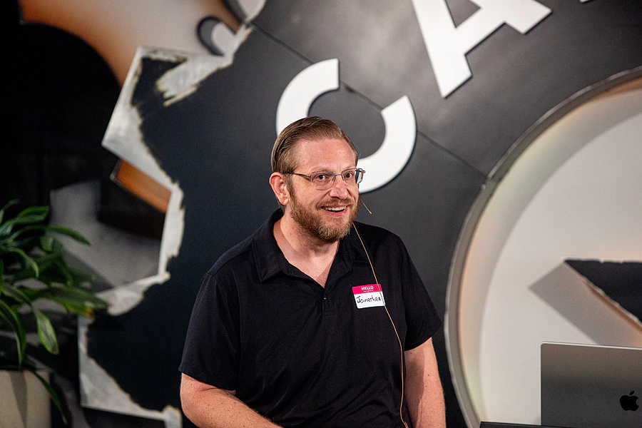 Jonathan Malkin speaking at an event in Austin, wearing a name badge and a headset microphone.