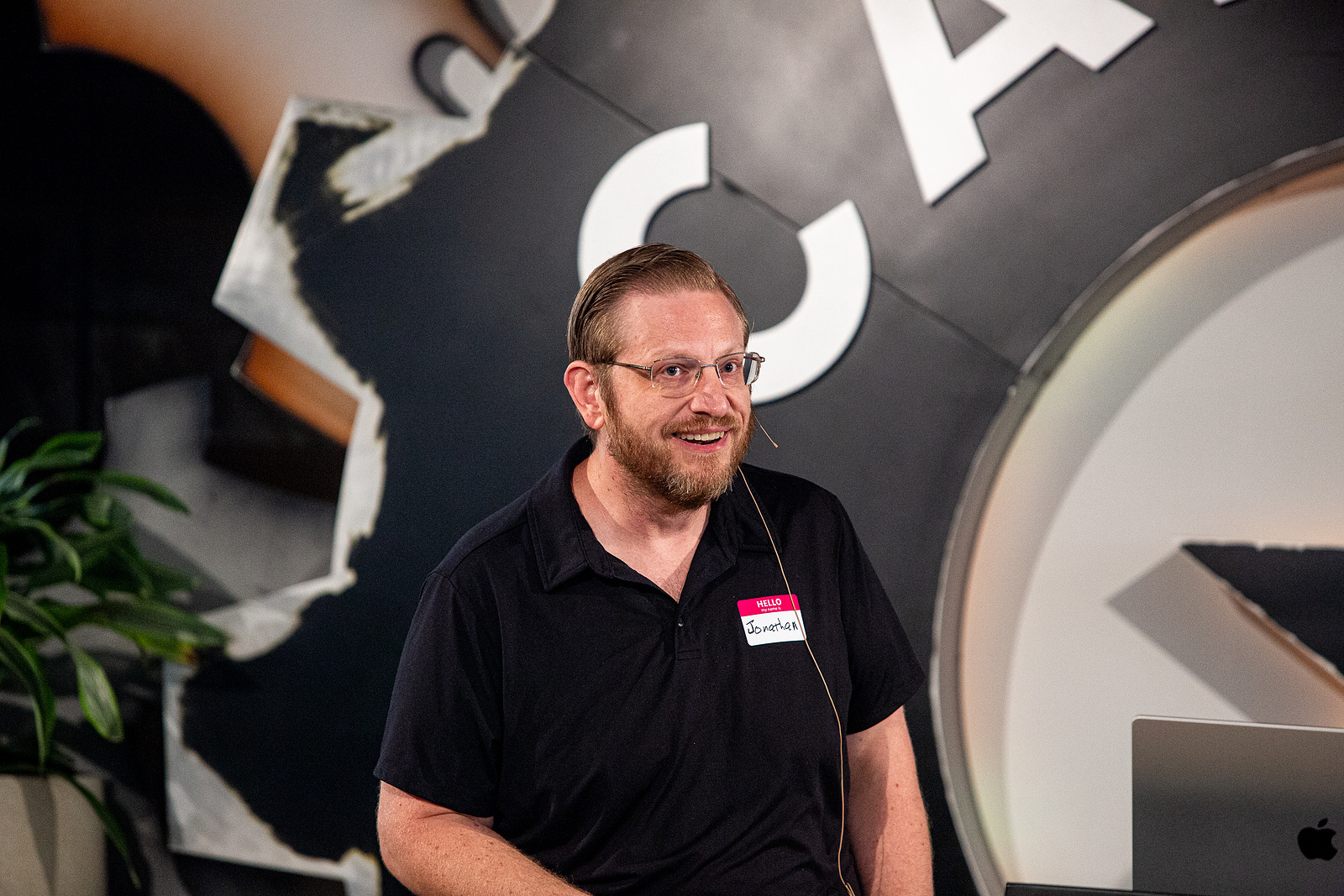 Jonathan Malkin speaking at an event in Austin, wearing a name badge and a headset microphone.
